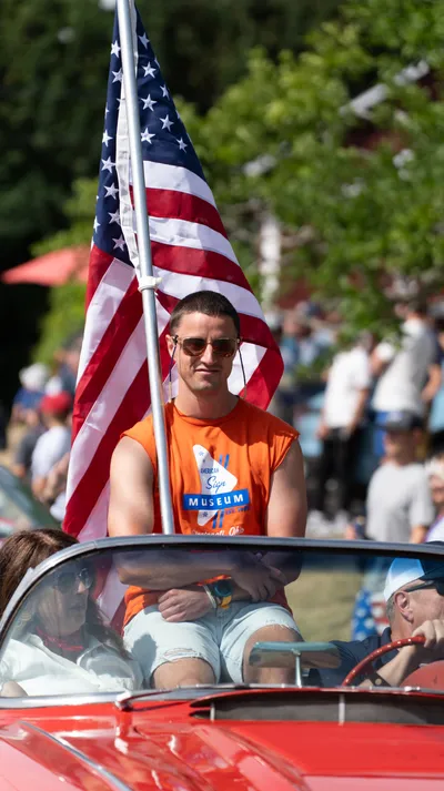 A young man holds an American flag while riding in a convertible during the Fourth of July parade in Home, Washington.